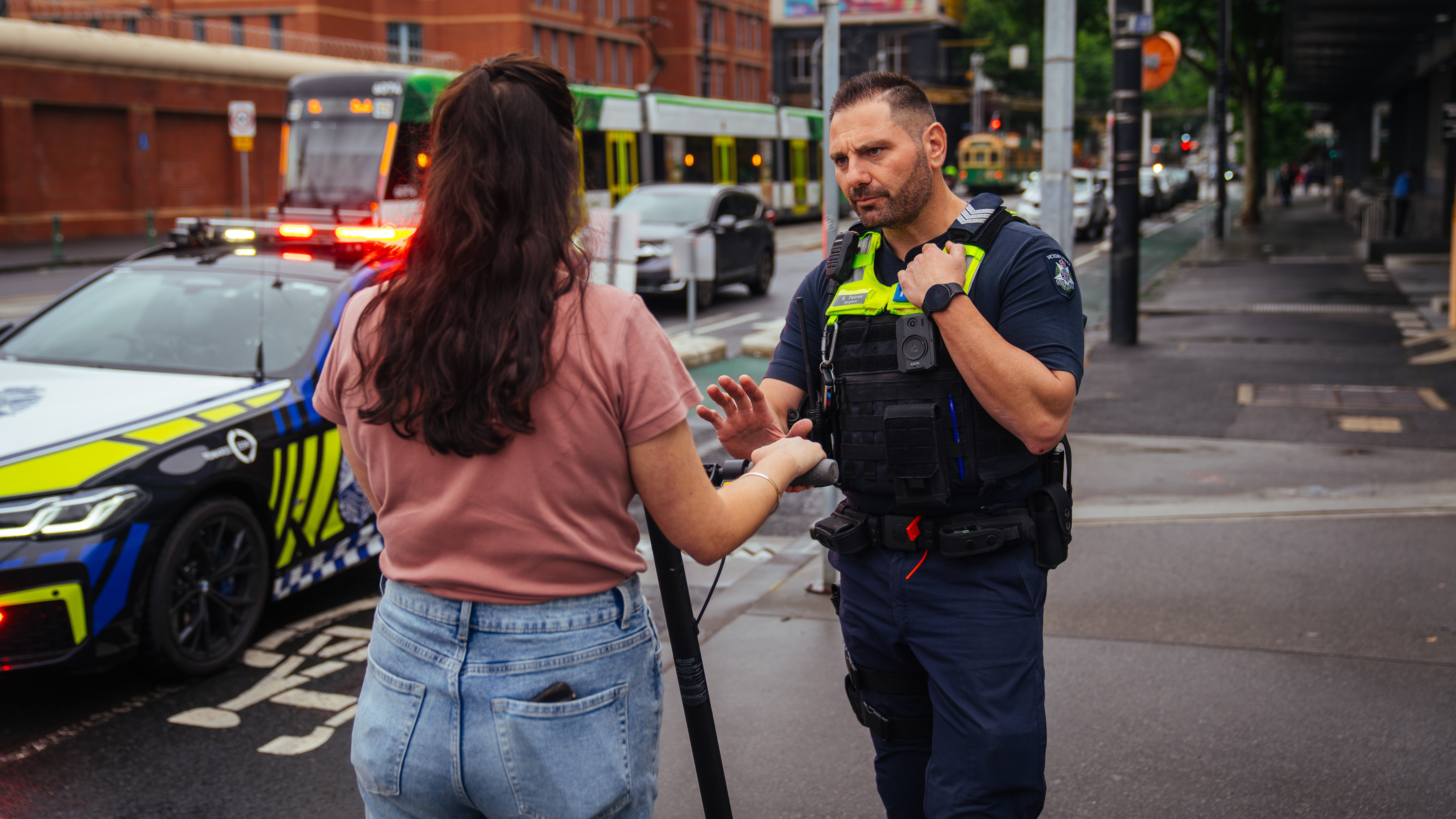 A police officer stopping a member of the public riding an e-scooter on the footpath.